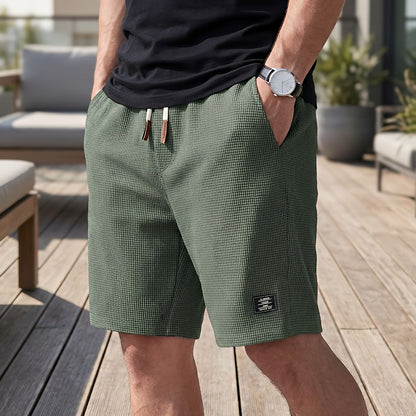 Model wearing olive green waffle-textured shorts with drawstring waist, one hand in pocket, on a wooden deck 5