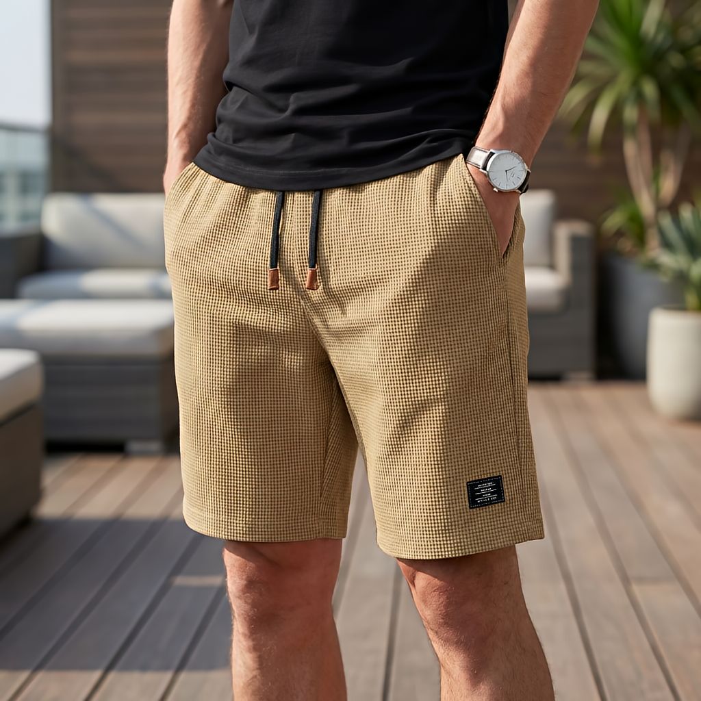 Model wearing khaki waffle-textured shorts with black drawstring and leather-tipped ends, standing on a terrace with a black 4