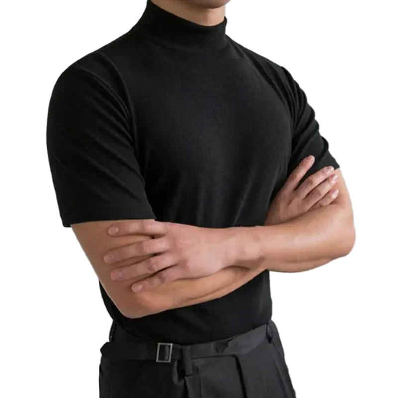 Model in a black short-sleeved mock-neck top with arms crossed, worn with dark belted trousers, on a white background 1
