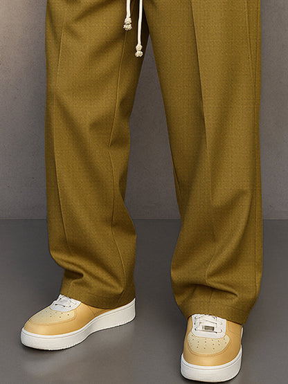 Close-up of the lower legs in mustard olive, showing the straight wide hems, front creases and cream and yellow trainers. 8