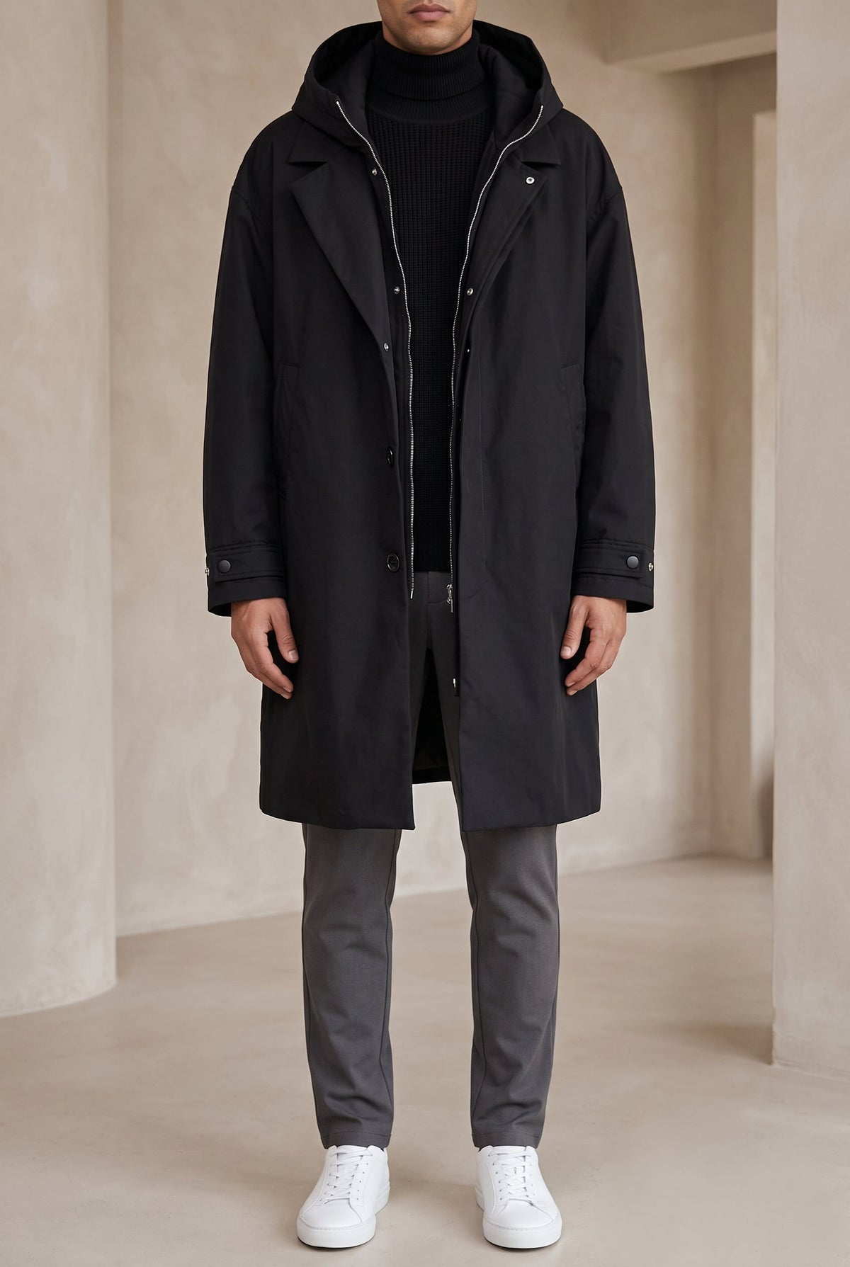 Model wearing the black hooded coat open over a black knit and grey trousers, front view 6