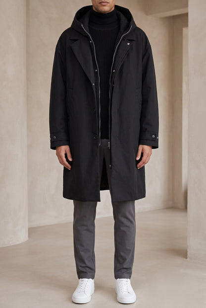 Model wearing the black hooded coat open over a black knit and grey trousers, front view 6