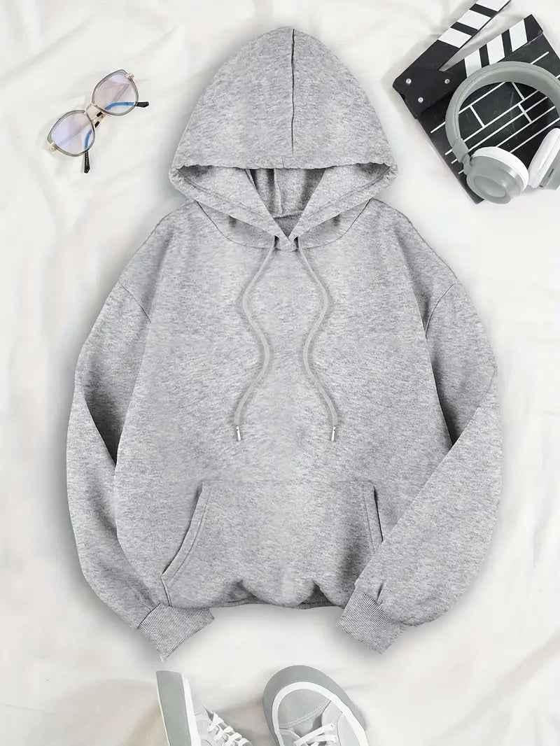 Front of the grey hoodie laid flat, showing the drawstring hood, kangaroo pocket and ribbed cuffs, with glasses, headphones and trainers. 4