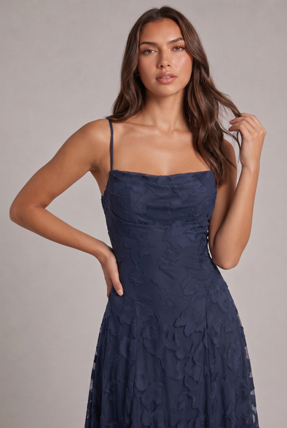 Close-up of the navy blue dress bodice on a model, showing the square cowl neckline and raised floral pattern. 18