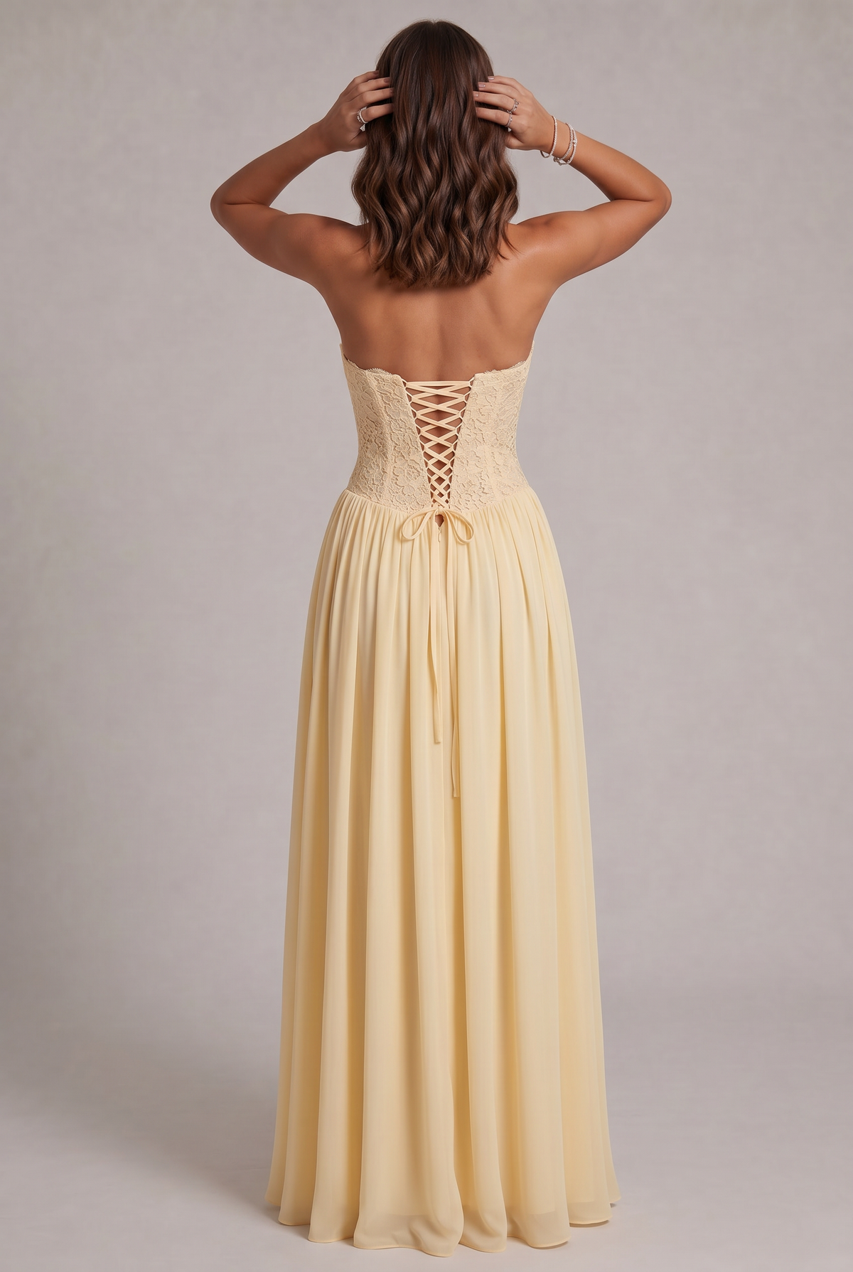 Back view of the pale yellow dress on a model, showing the lace-up corset back with bow and open shoulders. 8