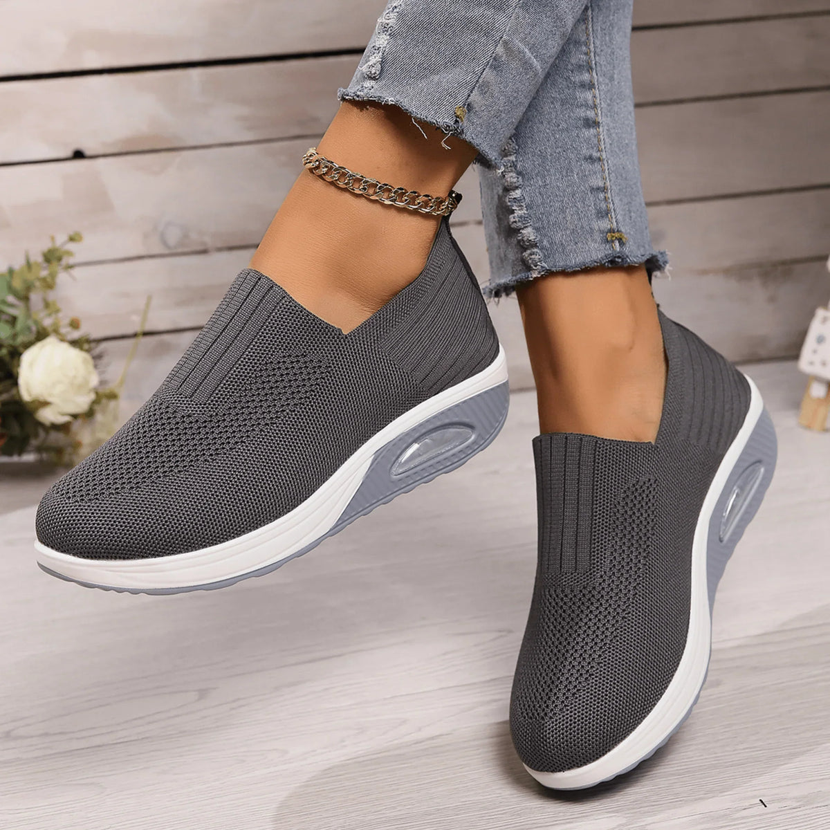 Dark grey knit slip-on trainers with white and pale grey soles, worn by a model with a gold chain anklet. 4