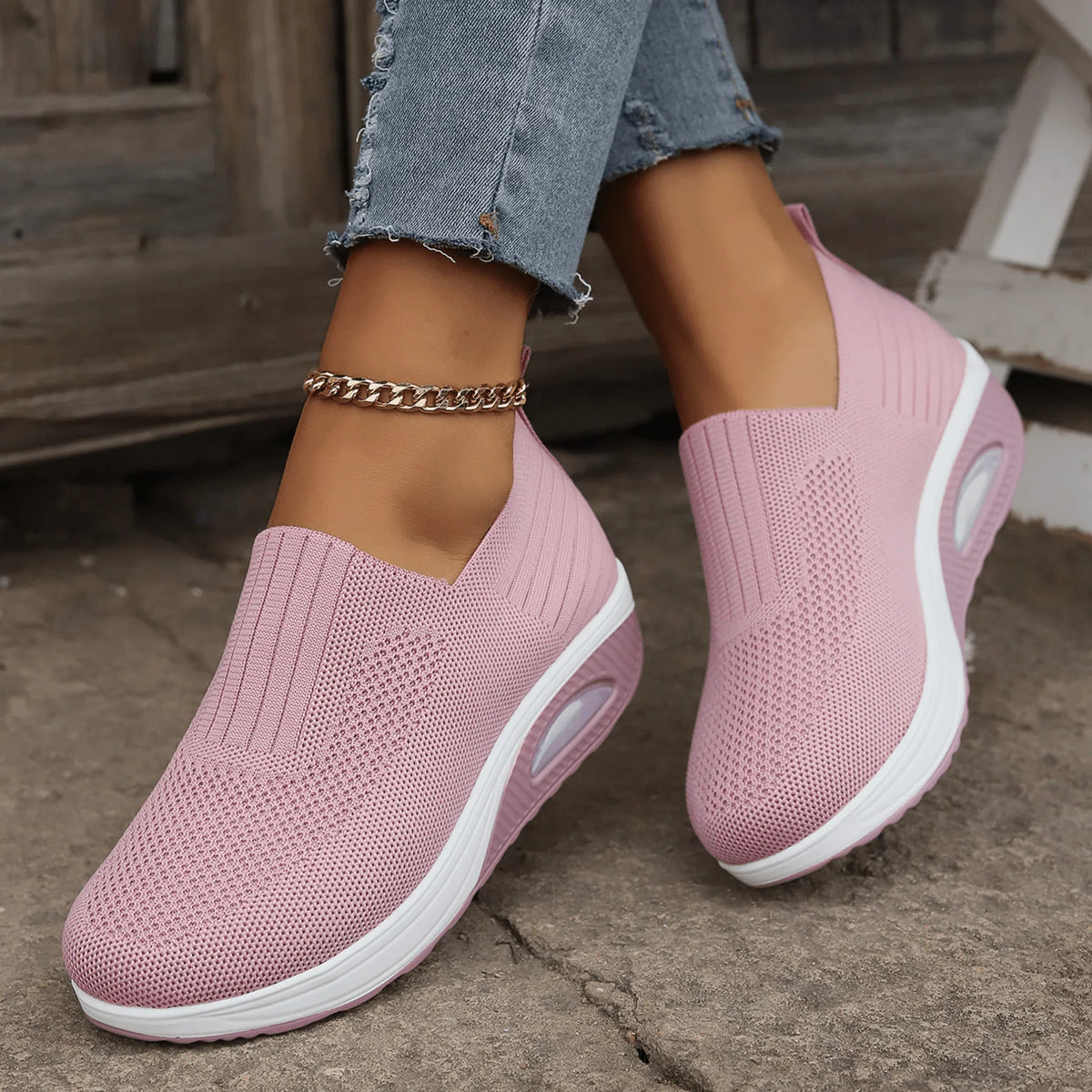 Pink knit slip-on trainers with white platform soles and air cushion, worn with frayed jeans on a stone surface. 5