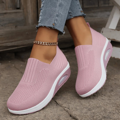 Pink knit slip-on trainers with white platform soles and air cushion, worn with frayed jeans on a stone surface. 5