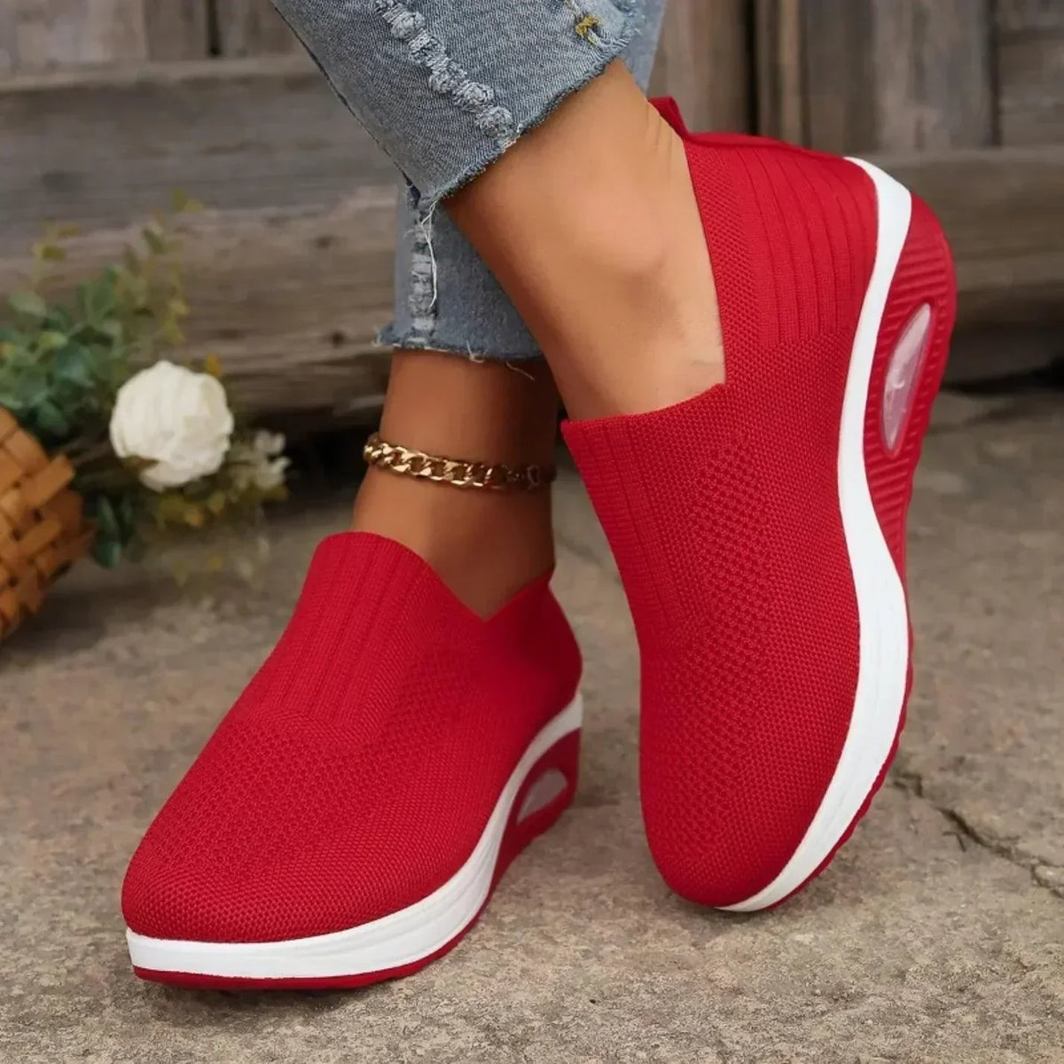 Red knit slip-on trainers with white soles and air cushion, worn by a model standing beside a white flower. 6