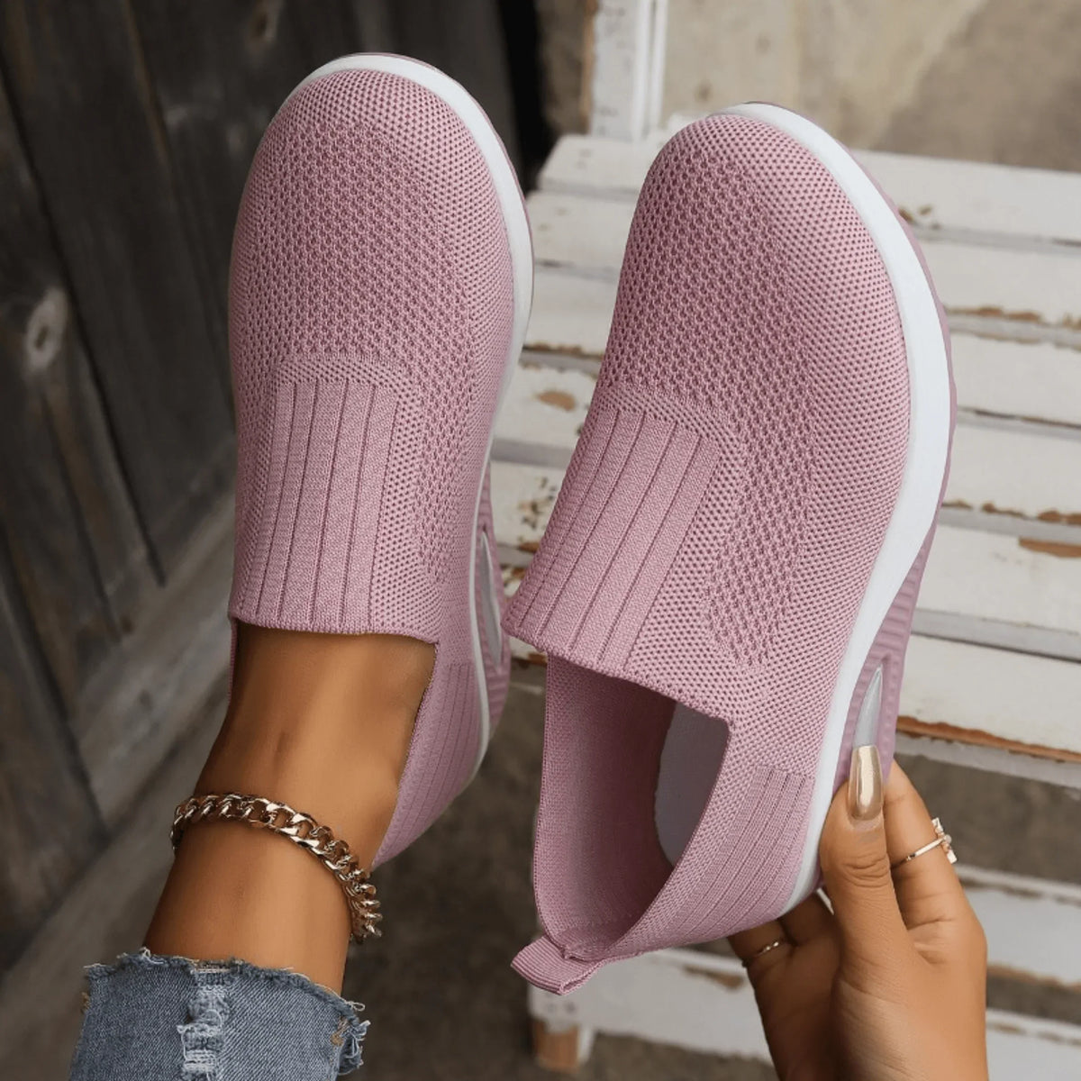 Top-down view of pink knit slip-on trainers showing the ribbed panels and mesh weave, one held in a hand. 7
