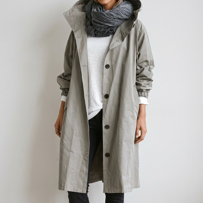 Model wearing the long button-up coat in light grey-green with the hood down, over a white top and grey scarf. 2