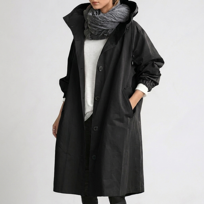 Model wearing the long hooded button-up coat in black, hand in pocket, styled with a grey scarf and white top. 3
