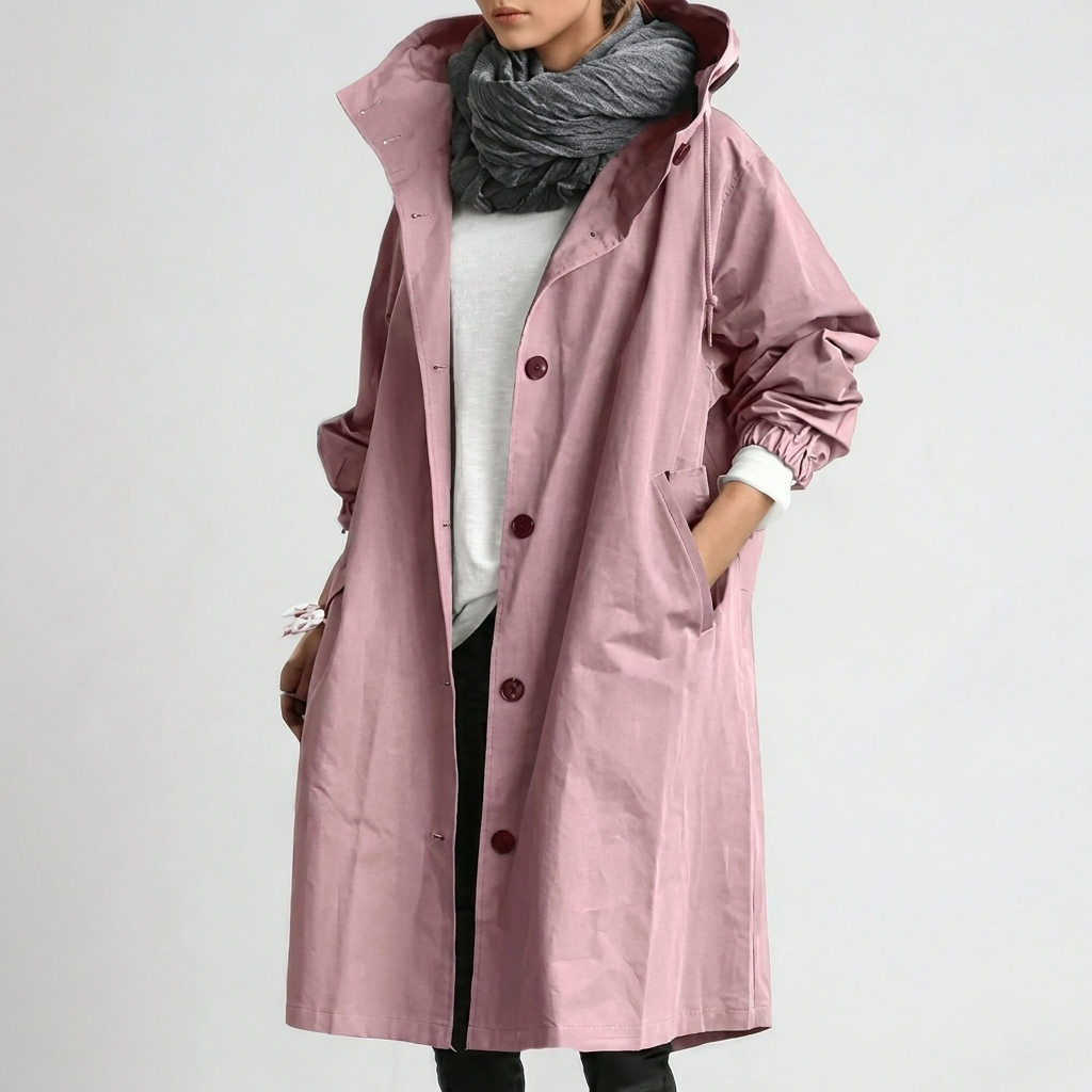 Model wearing the long hooded button-up coat in dusky pink, one hand in the pocket, with a grey scarf and white top. 1