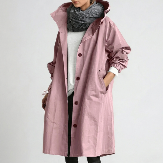 Model wearing the long hooded button-up coat in dusky pink, one hand in the pocket, with a grey scarf and white top. 1