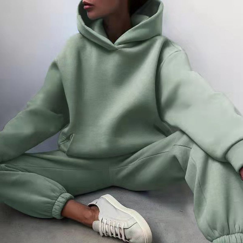 Model sitting on the floor in the sage green hoodie and cuffed joggers with elasticated ankles, wearing white trainers. 4