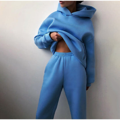 Model in the bright blue hoodie and elastic-waist joggers, hand tucked under the loose hem as she leans on a wall. 5