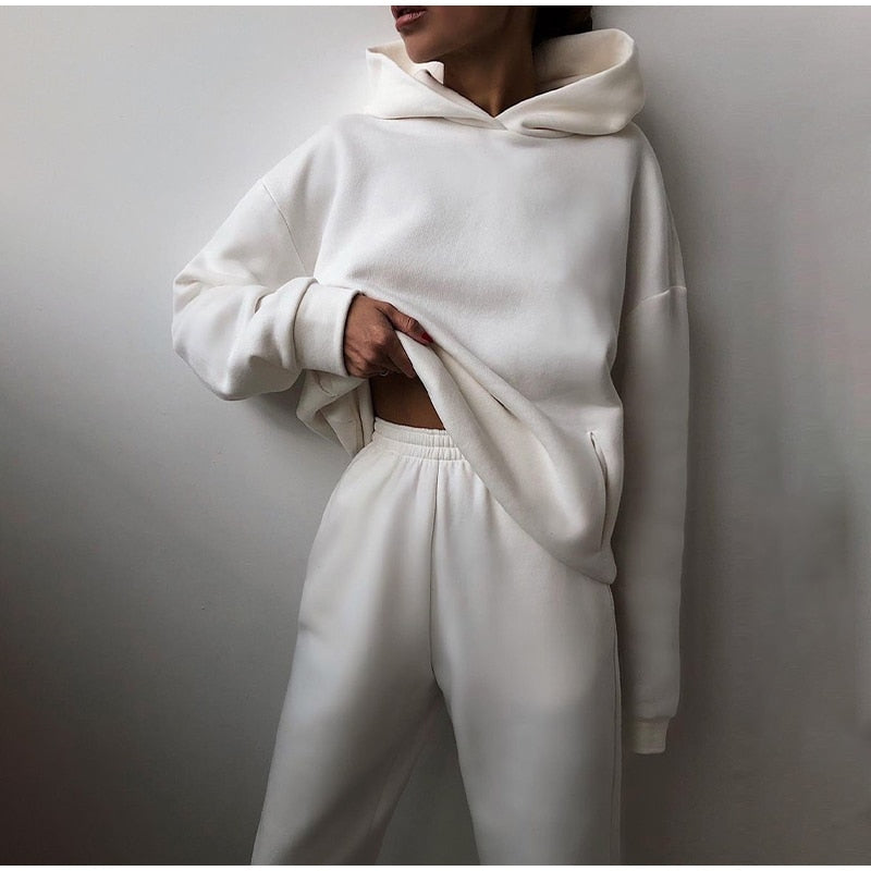 Model in the white hoodie and elastic-waist joggers, one hand pulling up the oversized hem to show the front pocket. 8