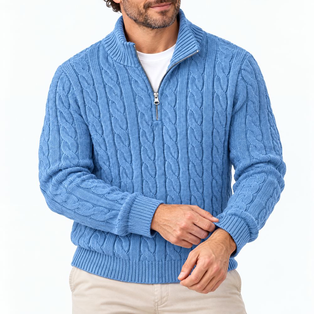 Close-up of a man wearing the blue cable knit jumper with the zip half open, ribbed cuffs, white tee and beige trousers. 1
