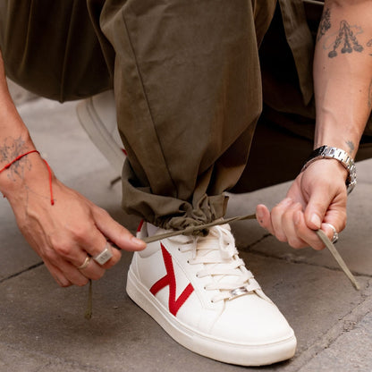 Close-up of a hand pulling the drawstring at an olive trouser ankle, worn over white trainers with red detail. 5