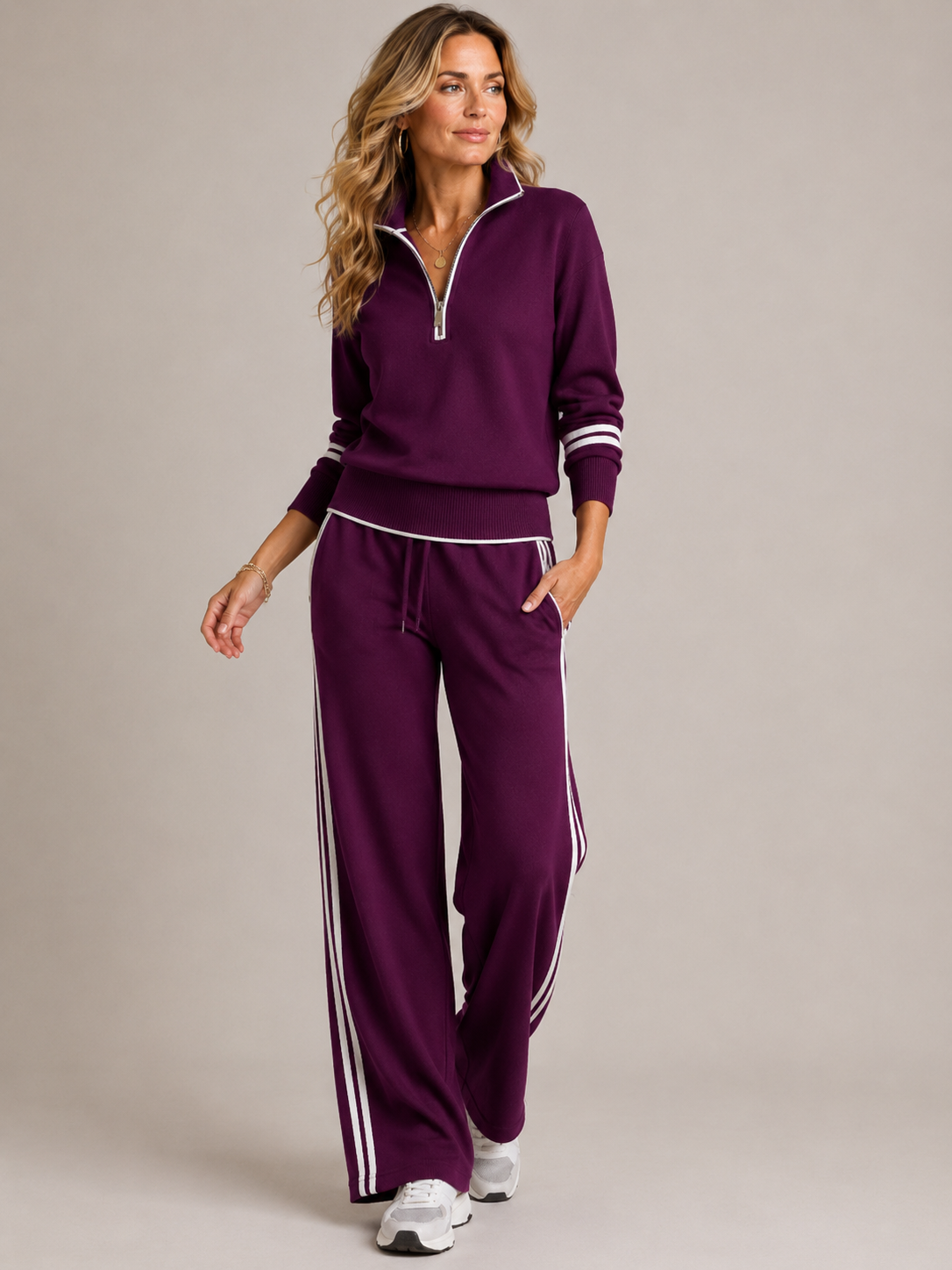 Model walking in the deep plum set with white piping and side stripes, worn with white trainers and gold jewellery. 2