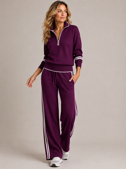 Model walking in the deep plum set with white piping and side stripes, worn with white trainers and gold jewellery. 2