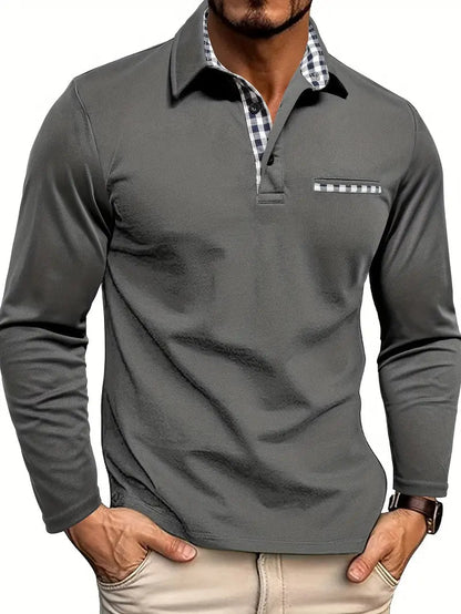 Man wearing the polo in charcoal grey, with black and white gingham trim on the collar, placket and chest pocket, hands in beige trousers. 2