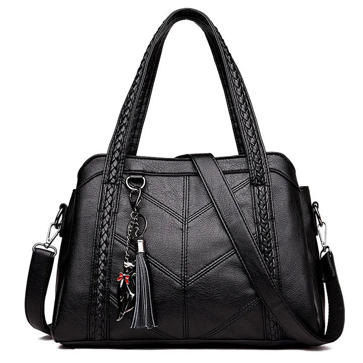 Black handbag on a white background, front view with braided handles, chevron stitching, shoulder strap, tassel and cat charm. 5