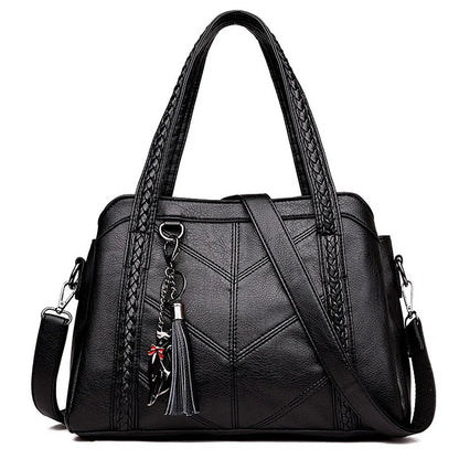 Black handbag on a white background, front view with braided handles, chevron stitching, shoulder strap, tassel and cat charm. 5