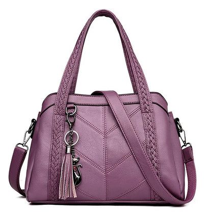 Purple handbag on a white background, front view with braided handles, chevron stitching, shoulder strap, tassel and cat charm. 6