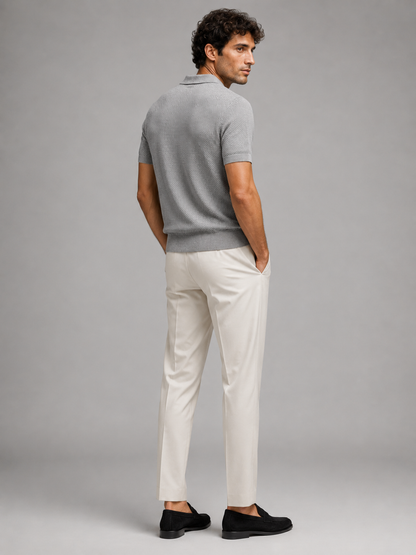 Back view of grey knit polo on model looking over shoulder, with cream trousers and black loafers 29