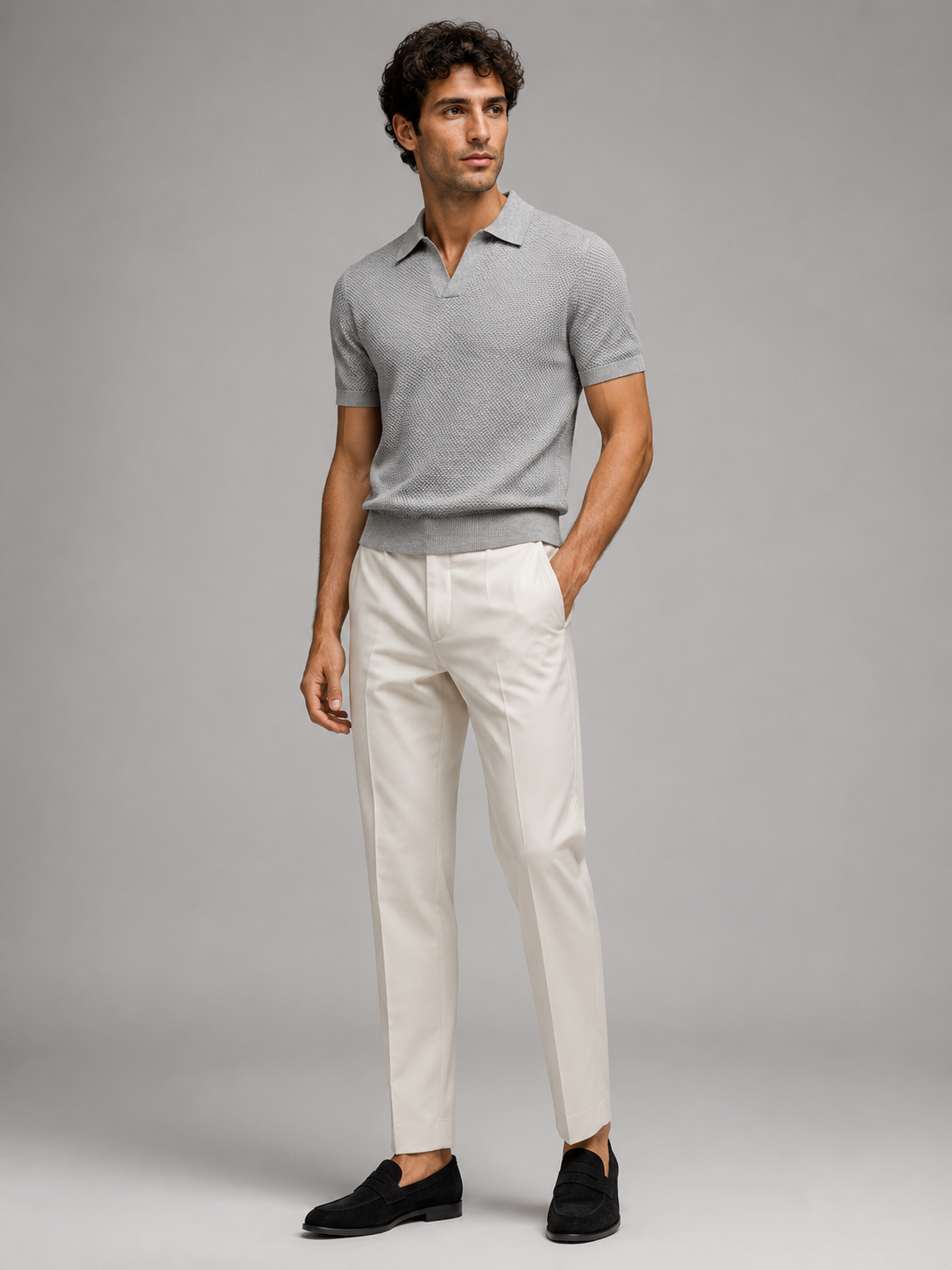 Full-length studio view of model in grey knit polo, cream trousers and black suede loafers 28