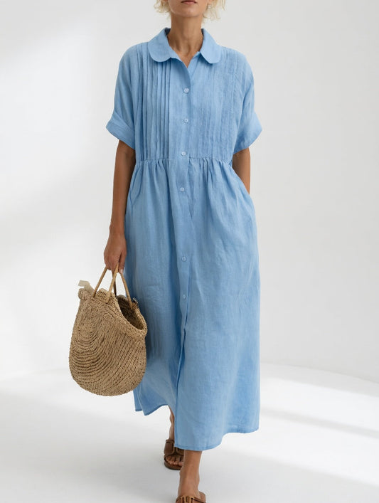Model in the pale blue dress facing front, showing the pleated bodice, round collar, full button front and cuffed short sleeves. 2