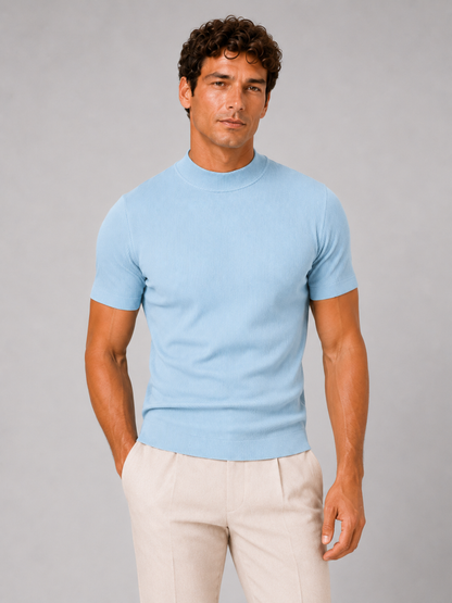 Front view of the light blue ribbed mock neck top, worn with cream pleated trousers against grey backdrop. 6