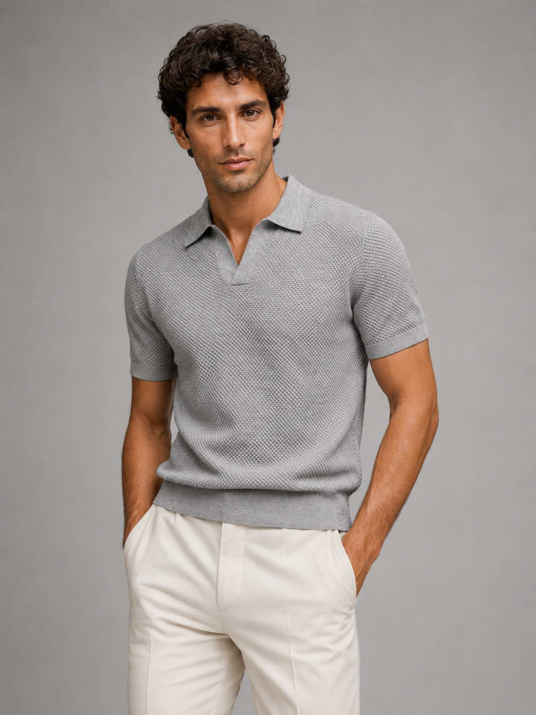 Model wearing light grey textured knit polo with open V-neck collar, hands in pockets, cream trousers, studio shot 26