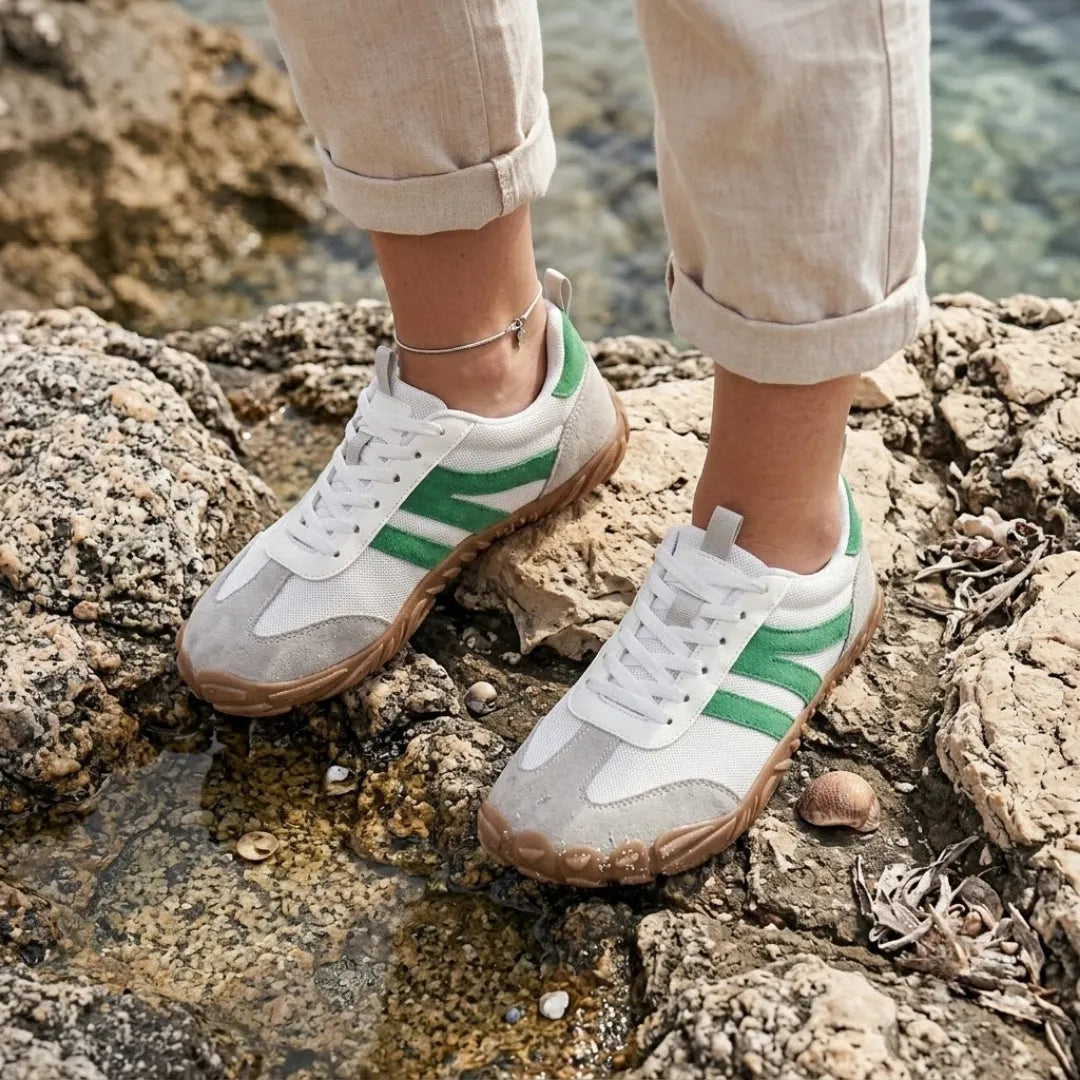 Woman wearing the white and green lace-up shoes while standing on rocks by shallow seawater, in rolled linen trousers. 29
