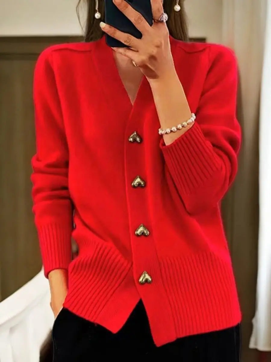 Bright red version of the cardigan worn by a model, showing gold heart buttons down the front and ribbed trim, with black trousers. 4