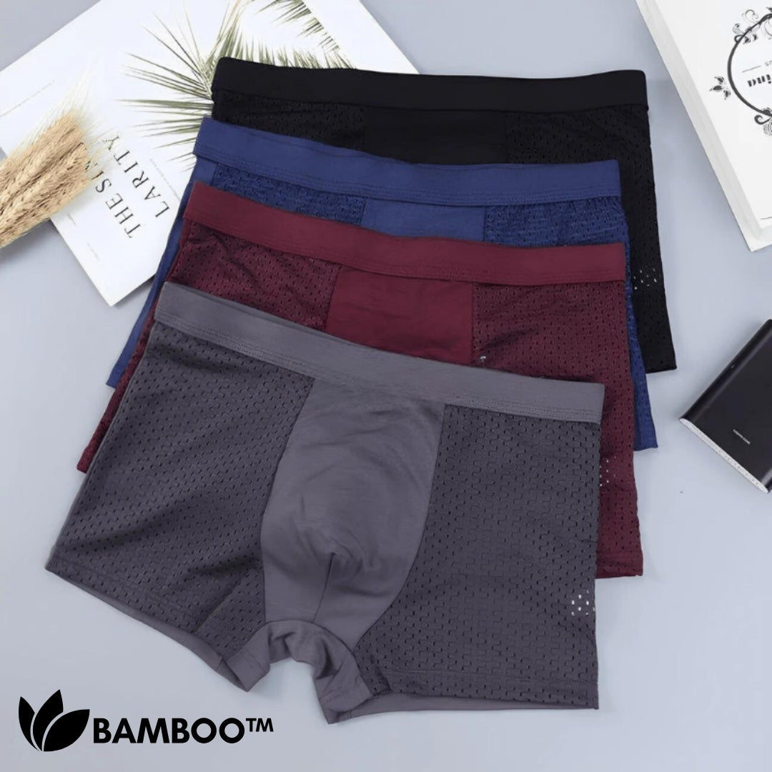 Flat lay of four stacked boxer briefs in black, navy, burgundy and grey, showing the mesh side panels on a pale surface. 3