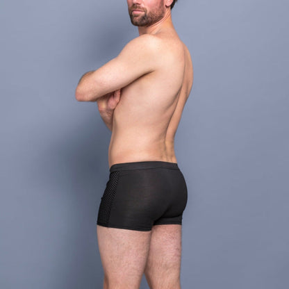 Bearded man with folded arms wearing black boxer briefs, photographed from the side and back against a grey-blue background. 7