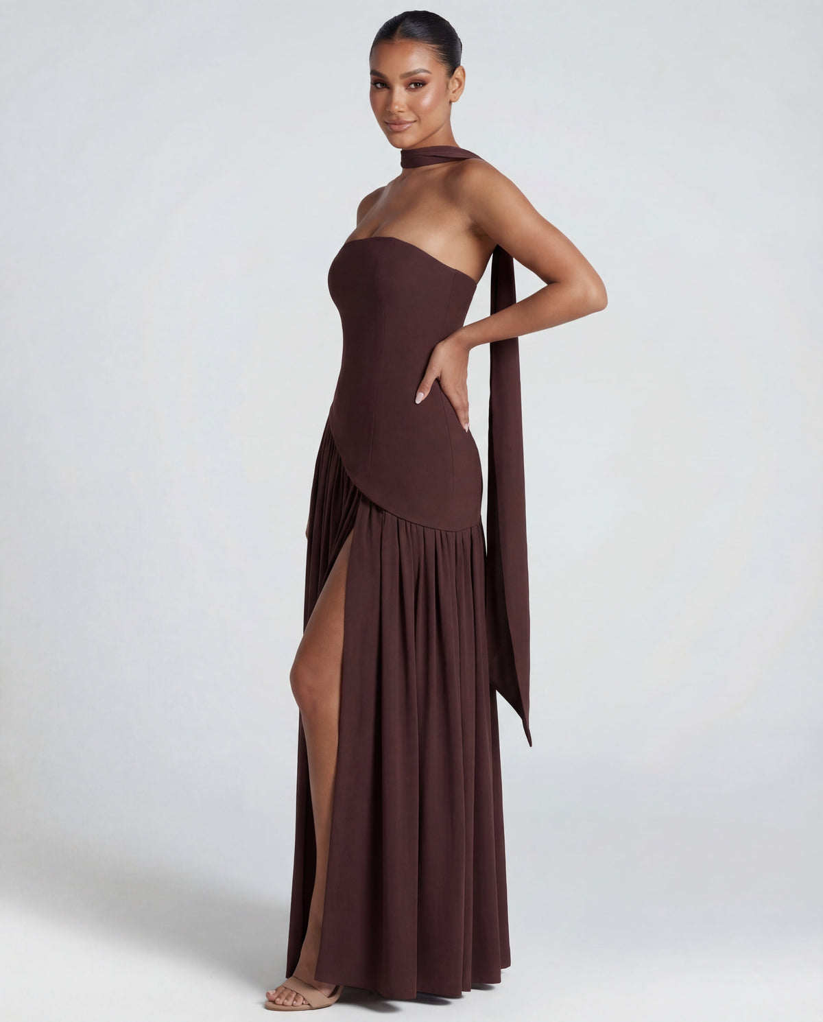 Side view of brown strapless maxi dress with scarf trailing from the neck and high leg slit 4