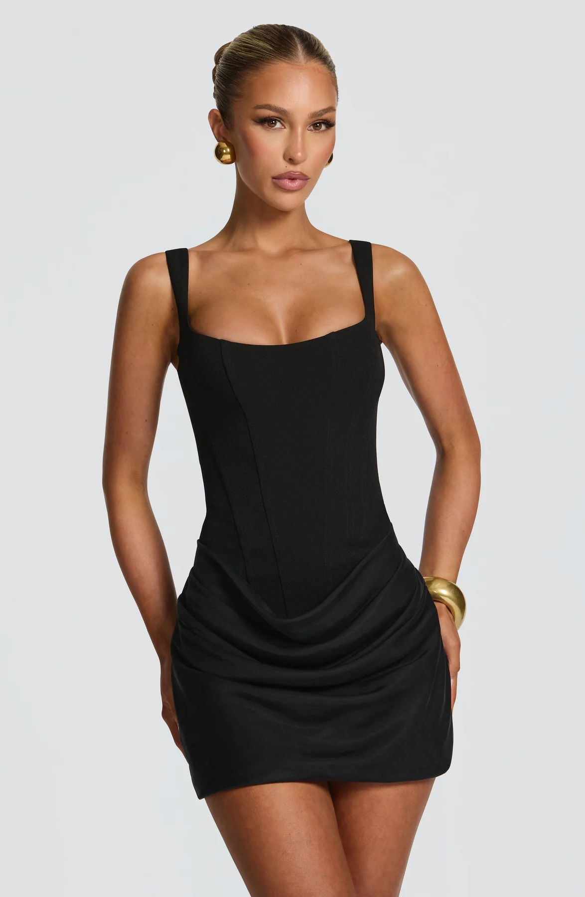 Close front view of the black dress on a model, with gold earrings and a bracelet, showing the corset seams. 5
