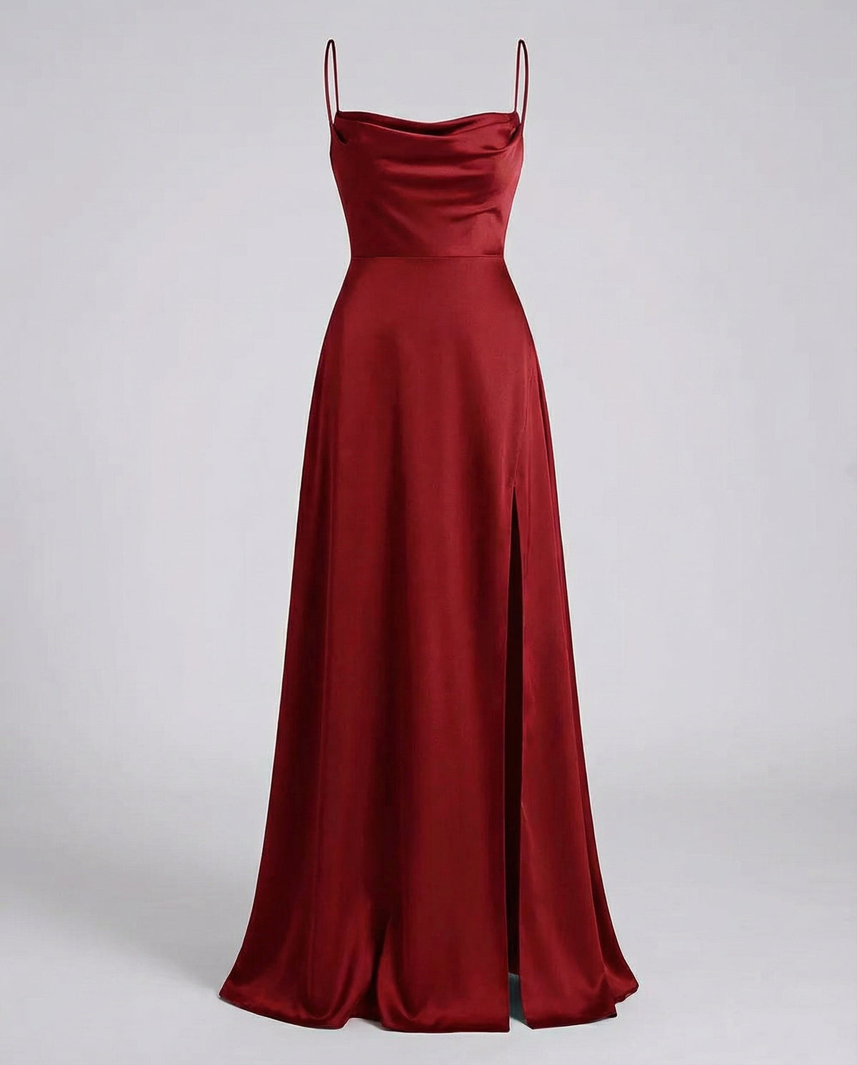 Burgundy satin maxi dress on a plain grey backdrop, showing the cowl neckline, thin straps, fitted waist seam and side slit. 2