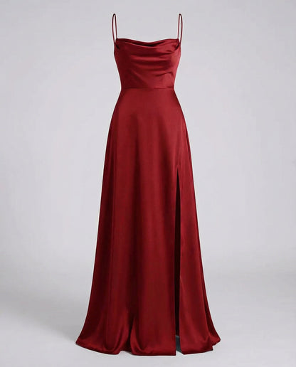 Burgundy satin maxi dress on a plain grey backdrop, showing the cowl neckline, thin straps, fitted waist seam and side slit. 2