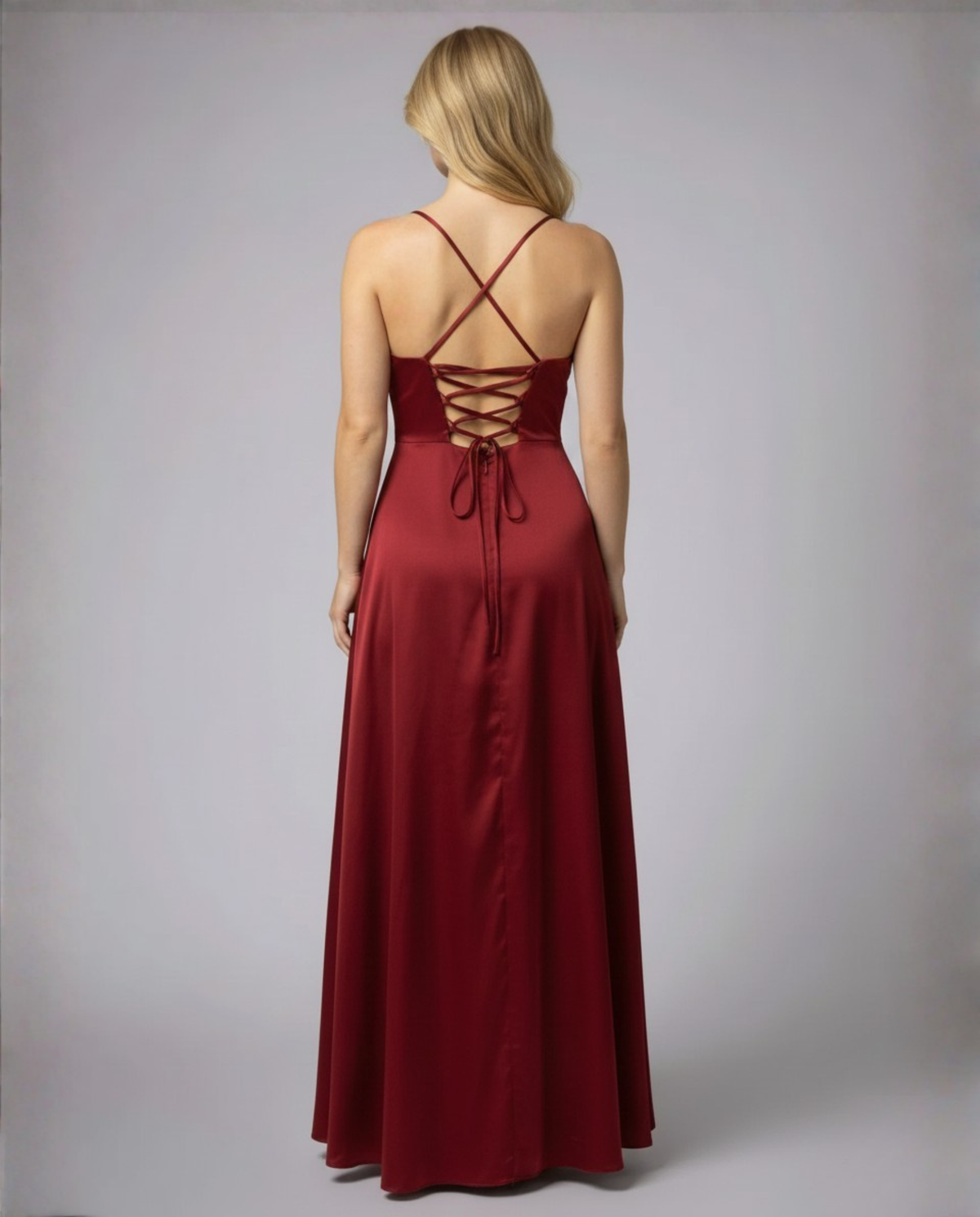 Back view of the model in the burgundy satin dress, showing crossed straps, a lace-up corset back and a long flowing skirt. 3