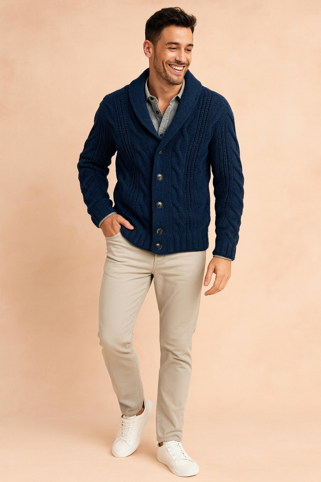 Full-length view of navy cardigan worn with stone trousers and white trainers on a peach backdrop 2