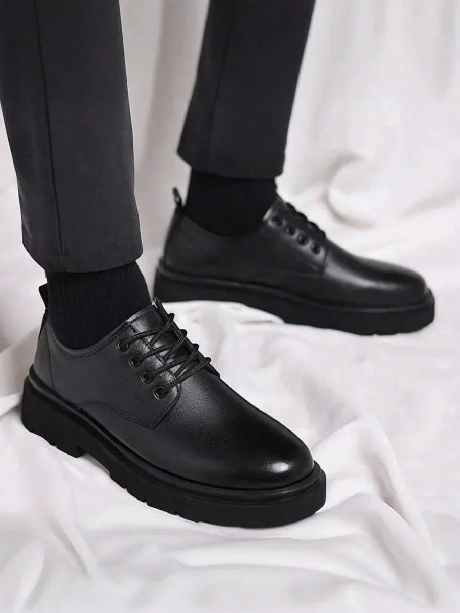 Black lace-up derby shoes worn with dark trousers and black socks, standing on white fabric 1