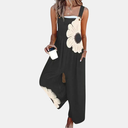 Model wearing black wide-leg dungarees with a large cream flower, holding a coffee cup, front view 1