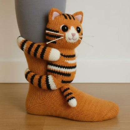 Orange knitted sock with a striped tabby cat figure hugging the ankle, shown worn indoors 3