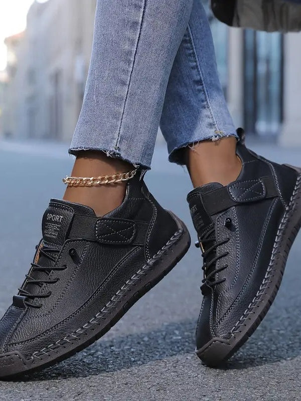 Black leather-look trainers worn by a model with a gold chain anklet and rolled jeans 5