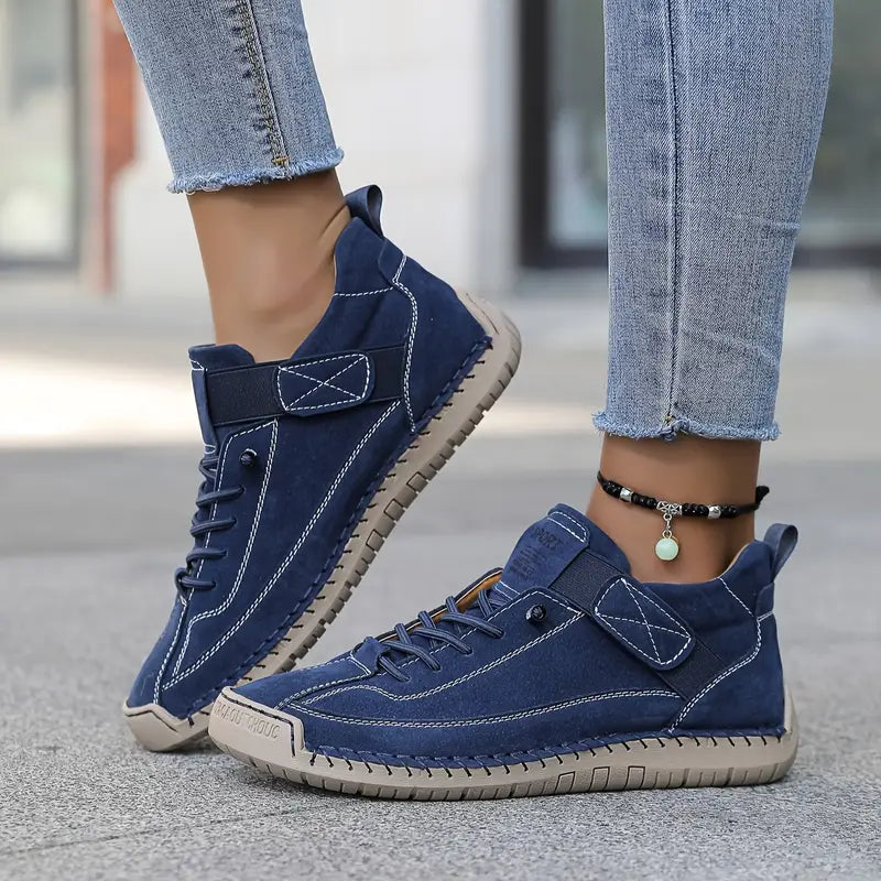 Navy blue suede-look trainers with white stitching and pale soles, worn outdoors with a beaded anklet. 7