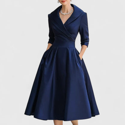 Navy blue version of the wrap-style midi dress with shawl collar and full pleated skirt, worn by a model with a crystal necklace. 2